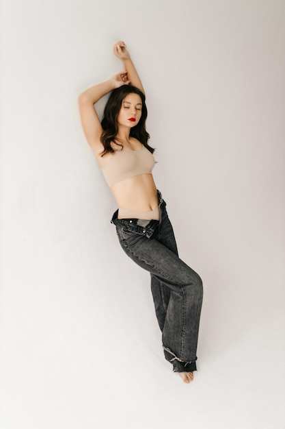 Young girl posing on a white background in a beige top and jeans