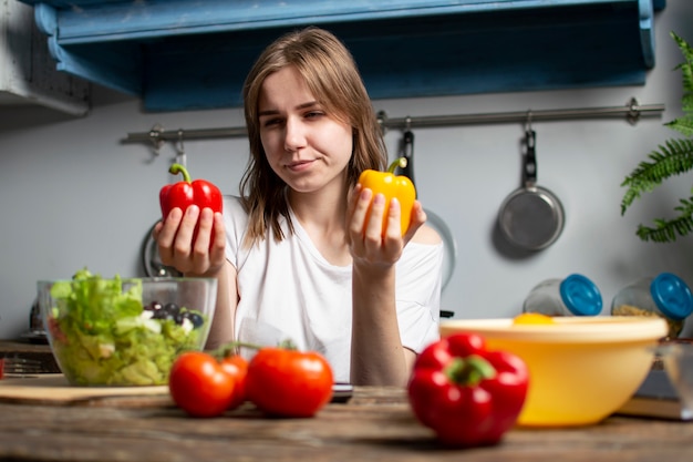 若い女の子が台所でベジタリアンサラダを準備し、彼女は赤または黄色のコショウ、健康食品を準備するプロセスを選択します