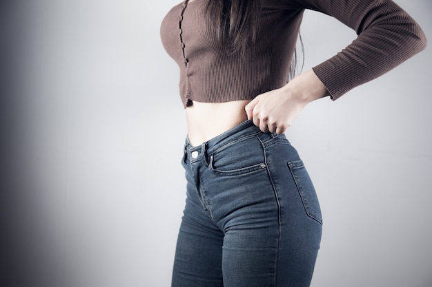 Young girl pulls jeans on a gray background