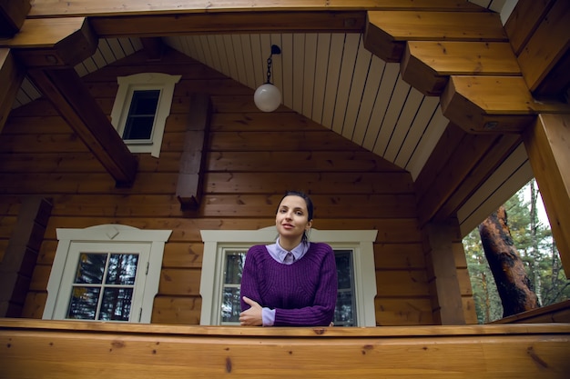 Young girl in a purple sweater and black jeans out on the porch of a wooden house