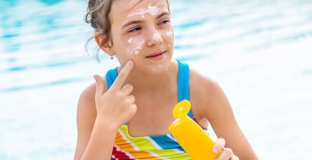 Young girl putting sunscreen on her face by the pool