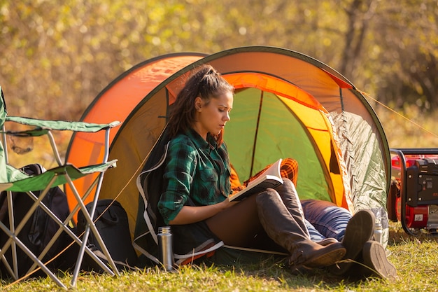 Young girl reading a book in front of the tent. Wild atmosphere