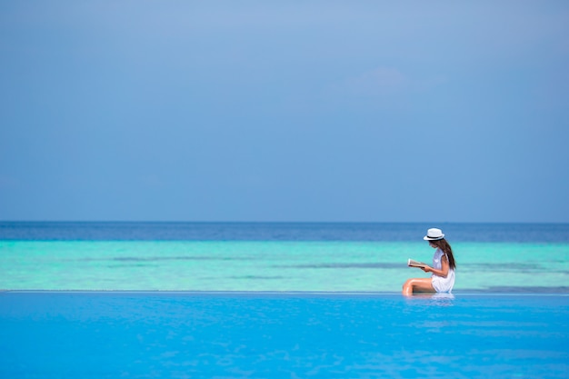 Young girl reading book near swimming pool