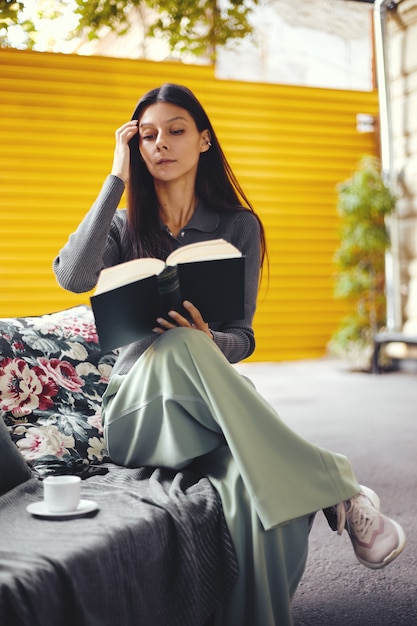 Photo young girl reading book while sitting at coffee shop with cup with hot