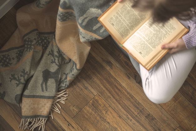 Young girl reading book while sitting in lotus pose on chair in cozy living room, concept of spending leisure time at home, cold winter season background photo