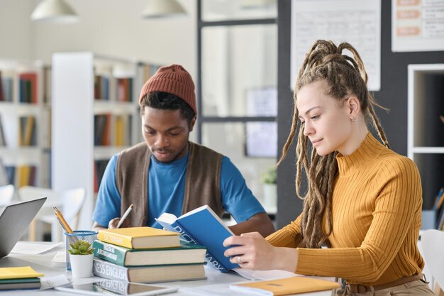 写真 クラスメートとテーブルに座り、図書館で試験の準備をしながら本を読む若い女の子