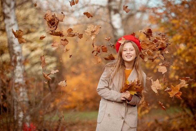 A young girl in a red beret and coat holds a bouquet of autumn leaves rejoices in autumn