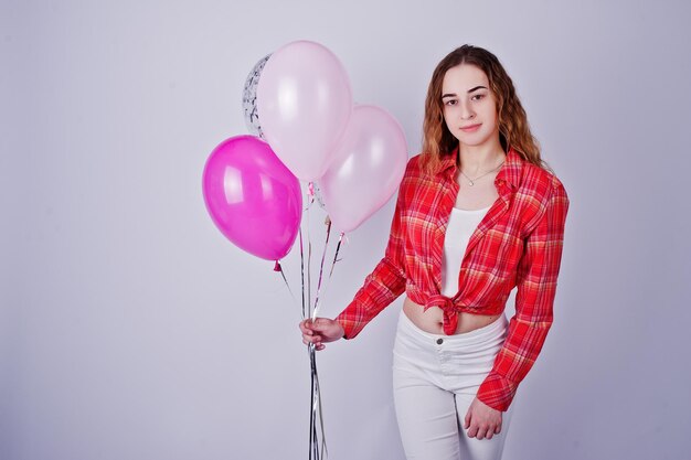 Young girl in red checked shirt and white pants with balloons against white background on studio