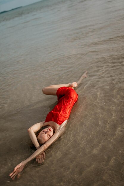 Photo a young girl in a red dress lies in sea water