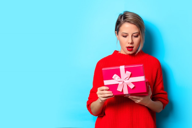 молодая девушка в красном свитере с подарочной коробкой