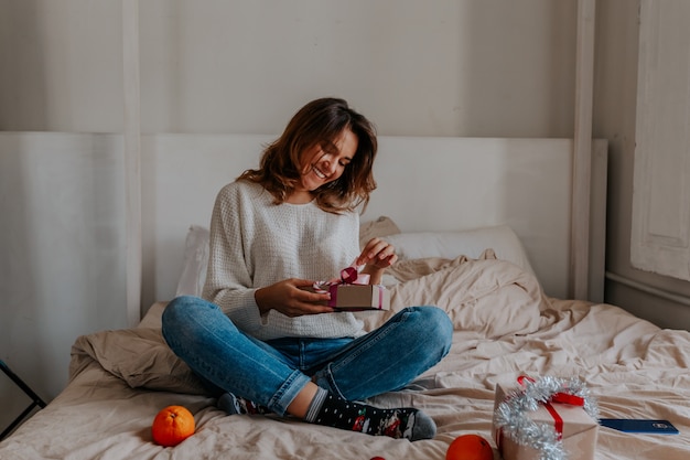 Young girl rejoices and holds a gift in her hands while sitting on the bed