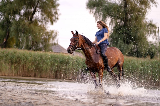 Una ragazza che monta un cavallo su un lago poco profondo. un cavallo corre sull'acqua al tramonto. cura e cammina con il cavallo. forza e bellezza