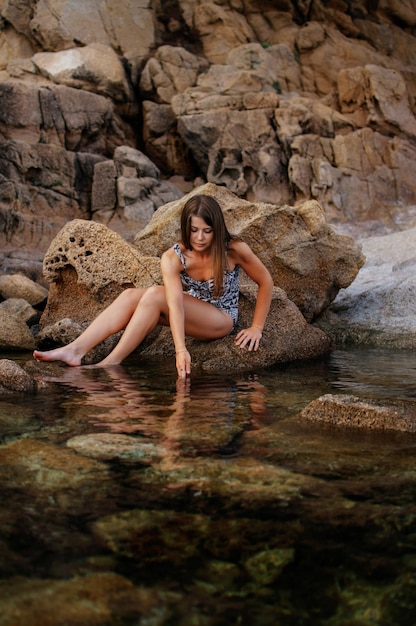 A young girl among the rocks looks into the water