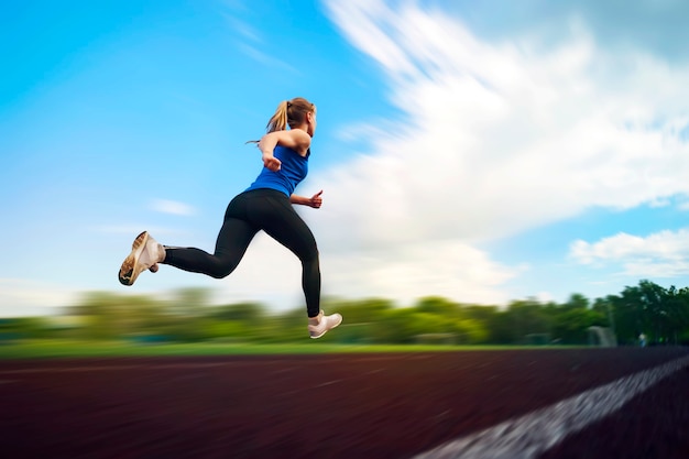 The young girl running in stadium, blur in moving. An athlete runs around the stadium jumping photo in flight. Athletics.