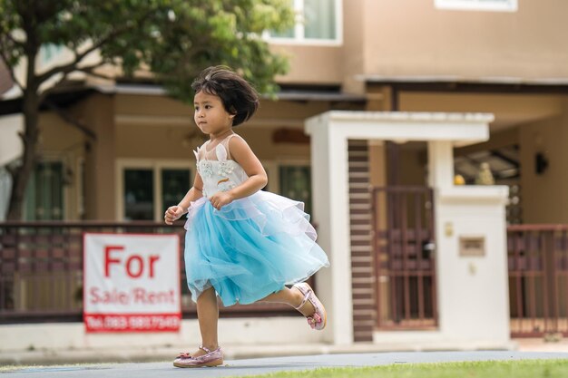 A young girl runs in front of a for sale sign