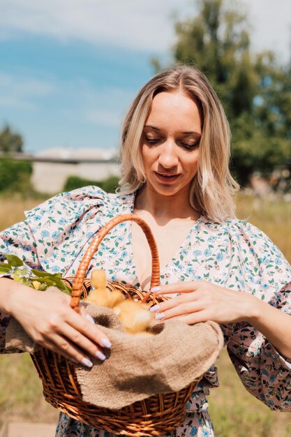 A young girl in a rural area holds a basket with ducklings in her hands