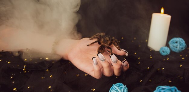 Young girl's hand with manicure and big spider with steam on black background Crop unrecognizable person with design on nails Concept of care and beauty