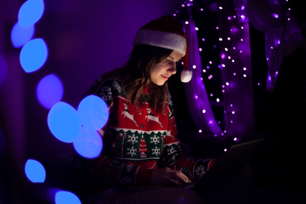 Young girl in a Santa Claus hat with a laptop