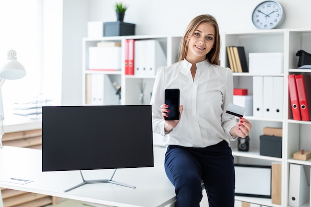 若い女の子がテーブルに座って、電話と銀行カードを持っています。