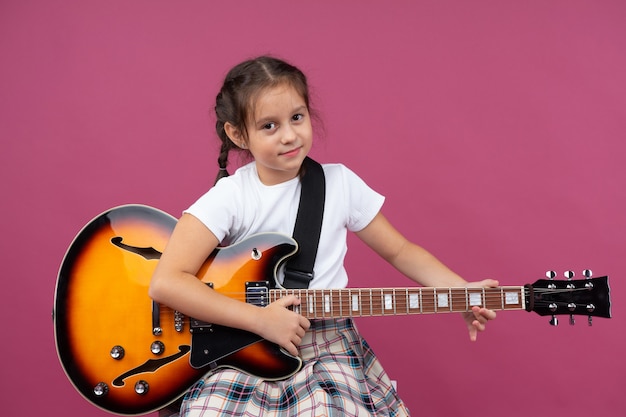 A young girl in a school uniform plays an electric guitar