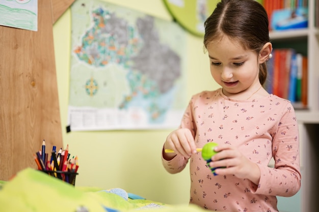 Young girl sharpening pencil in her room