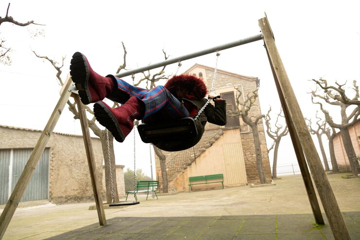 Photo young girl sheltered in an abandoned swing set with hood unrecognisable