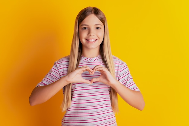 Young girl show fingers heart love sign chest isolated over yellow background