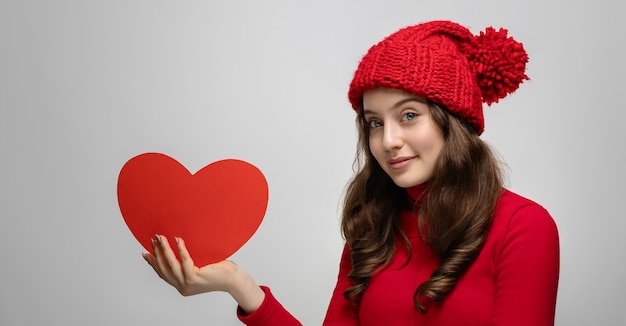 Young girl showing red heart from cardboard to camera, valentine's day