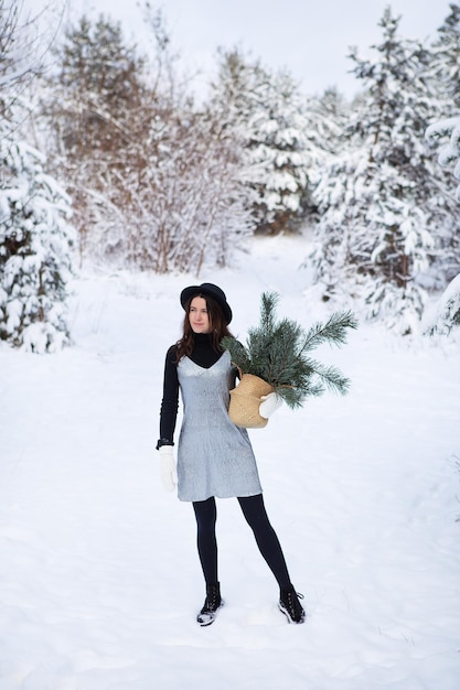 銀色のドレスと帽子をかぶった若い女の子が、美しい冬の森の真ん中に背中を向けて立っています。