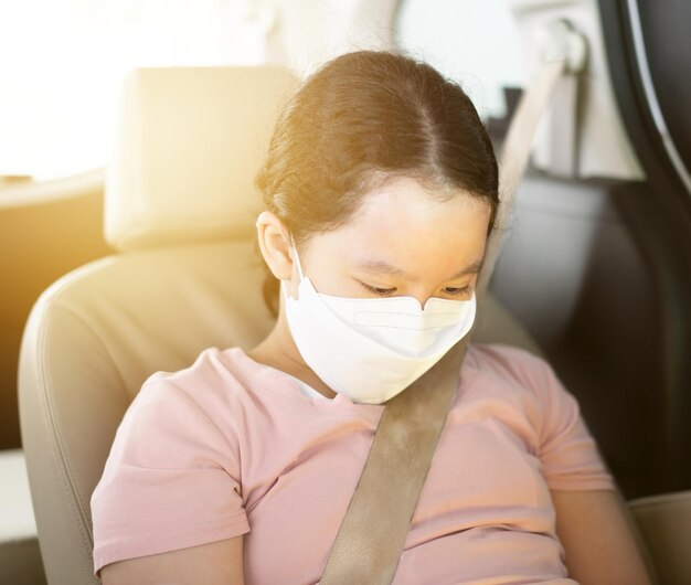 若い女の子は、covid検疫で保護マスクと車に座っています