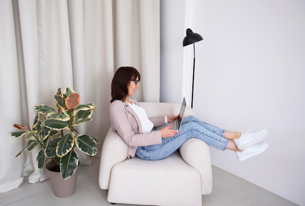 a young girl sits in an armchair at home with a laptop and talks on a video link and studies