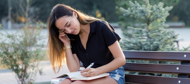 A young girl sits on a bench in a park and makes notes Dressed in a free style Business woman talking on the phone with customers