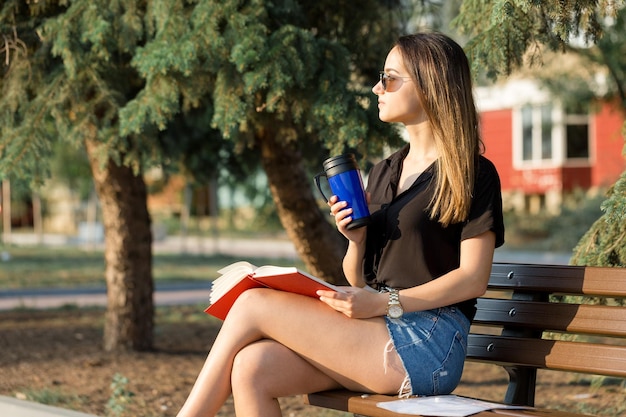 若い女の子が公園のベンチに座ってメモをとるフリースタイルの服を着て顧客と電話で話しているビジネスウーマン