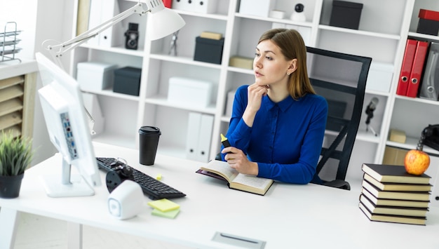 若い女の子がコンピューターの机に座っていると彼女の手に黄色のマーカーを保持しています。