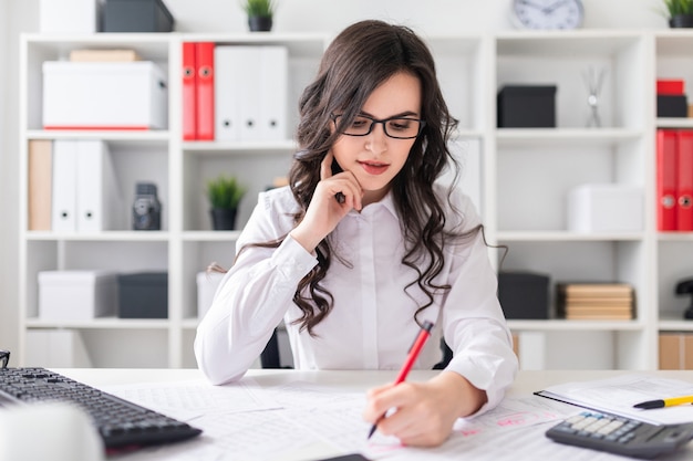 Photo young girl sits at office desk and fills documents with her left hand.