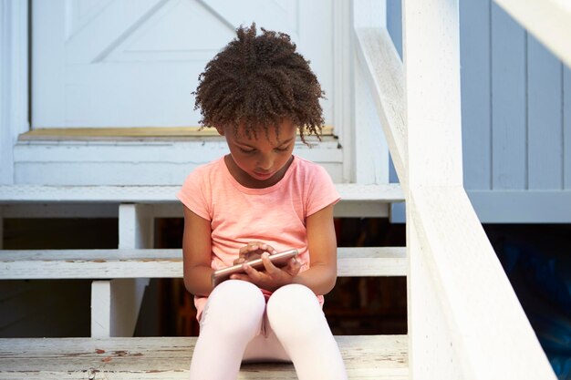 어린 소녀는 휴대 전화를 가지고 노는 야외 단계에 앉아