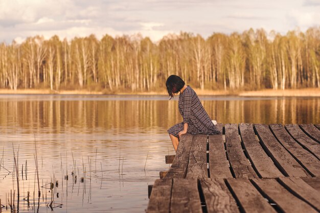 Young girl sits on a pier in a summer dress