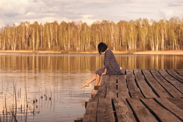 Young girl sits on a pier in a summer dress