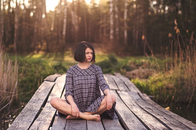 Photo young girl sits on a pier in a summer dress