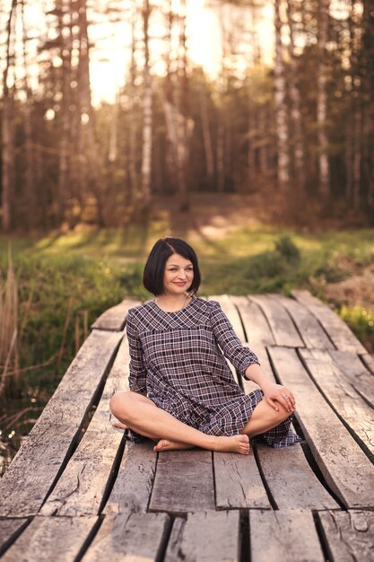 Photo young girl sits on a pier in a summer dress