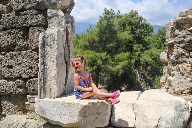 Foto una ragazzina si siede su una roccia con una visiera solare rossa sulla testa