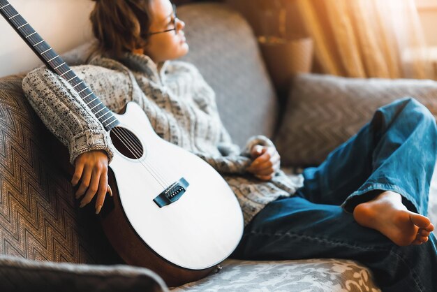 Young girl sits in room on couch with guitar Teenager is hipster with musical instrument