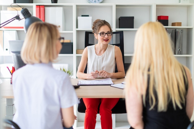 A young girl sits at a table in her office and talks to two co-partners.