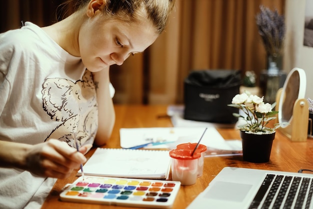 Young girl sits at table in her room and paints with watercolor paints Theme of creativity inspiration and drawing