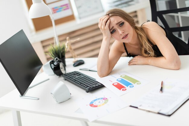 A young girl sits at a table in the office and propps her hand on her head.