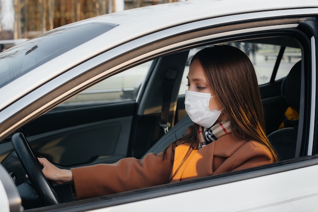 A young girl sits behind the wheel in the car in the mask during the global pandemic and coronavirus. Quarantine.