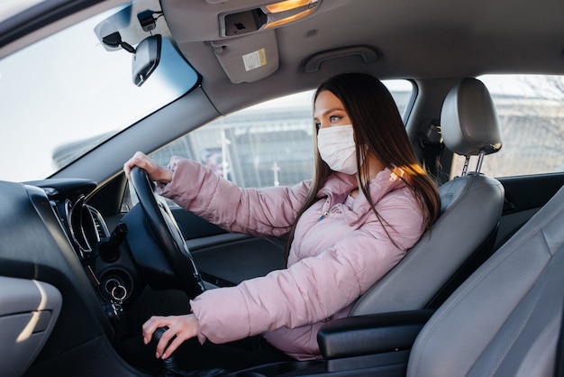 A young girl sits behind the wheel in the car in the mask during the global pandemic and coronavirus. Quarantine.