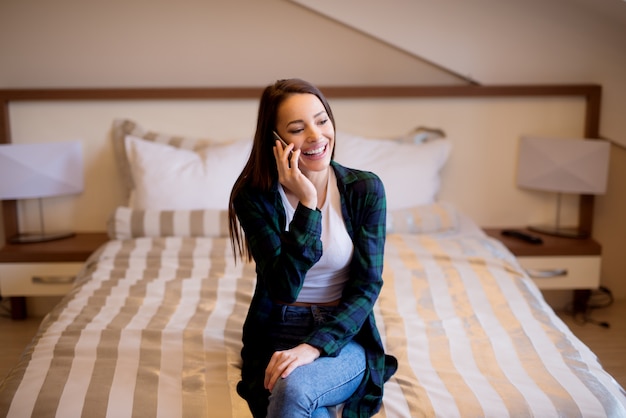 Young girl sitting on the bed and talking on the phone.