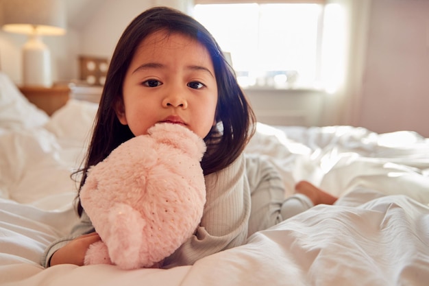 Young Girl Sitting On Bed Wearing Pyjamas At Home Cuddling Soft Toy