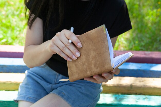 A young girl sitting on a bench makes notes in a diary